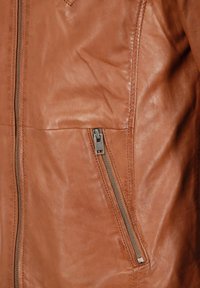 Bruine leren jas met een gladde textuur, een ritszak aan de zijkant en contrasterende stiksels langs de naden.