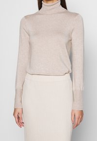 Pull en col roulé beige fabriqué à partir d'un tissu doux, avec des manches longues et une coupe ajustée, associé à une jupe tricotée à côtes assortie.