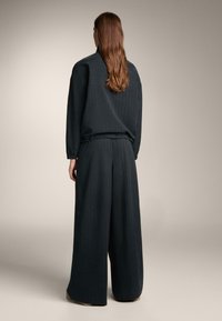 Fekete tűcsíkos kétdarabos öltözet laza felsővel és bő szárú nadrággal, elasztikus derékpánttal és hosszú ujjakkal.