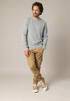 Grijze blouse met lange mouwen en khaki cargobroek, met zakken en taps toelopende manchetten, gecombineerd met tan sneakers met witte zolen.