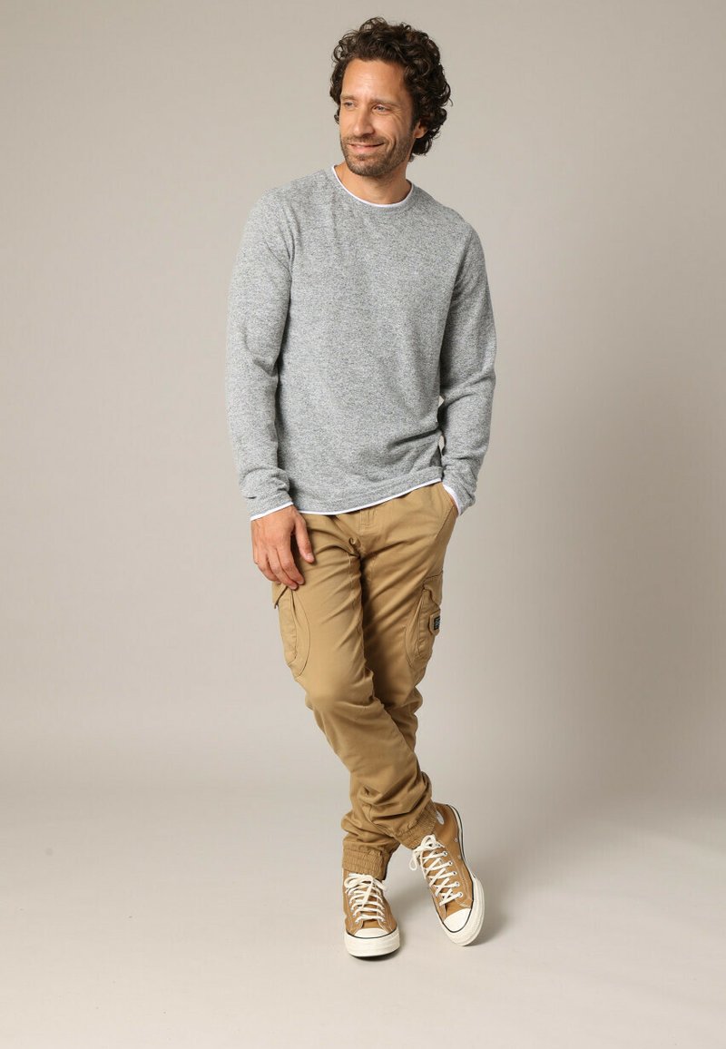 Graues Langarmhemd und khakifarbene Cargo-Shorts mit Taschen und schmal zulaufenden Bündchen, kombiniert mit braunen Sneakers mit weißen Sohlen.