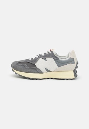 Szare i białe zamszowe sneakersy z kremową podeszwą, fakturowanym logo "N" oraz wytrzymałą czarną gumową podeszwą, pokazane z prawej strony na białym tle.