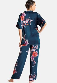 Floral print slaapset in donker teal satijn. T-shirt met korte mouwen en rugstrik, wijde broek met kleurrijke bloemmotieven. Zachte textuur.