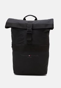 Sac à dos noir à rouleau fabriqué en tissu texturé, équipé d'une sangle réglable, d'une poche zippée à l'avant et d'un panneau logotypé en bas.