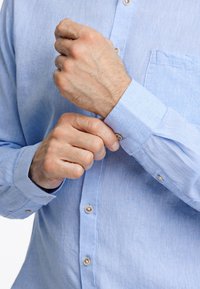 Lichtblauw overhemd met knopen van een textuurstof, met een zak en contrasterende knopen op de mouwen en de voorkant.