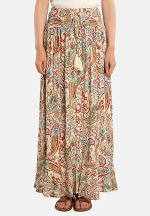 Donna che indossa una gonna lunga e fluida con motivo paisley multicolore e vita con coulisse, abbinata a sandali marroni e top bianco.