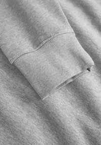 Gros plan sur un tissu de sweat-shirt gris, présentant une finition lisse et texturée avec un poignet replié et des détails de couture visibles.