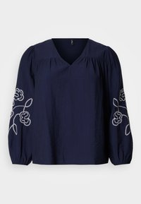 Blouse marine avec un col en V, manches longues bouffantes ornées de broderies florales blanches le long des poignets. Tissu doux avec une coupe décontractée.