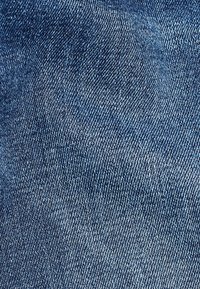 Denimtyg i en ljus till medelblå nyans, med en texturerad väv och subtila blekningar för djup och visuell intress.