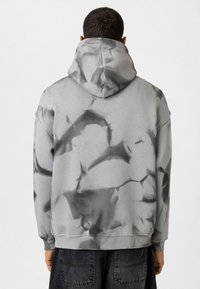 Grijze hoodie met zwart tie-dye patroon, gemaakt van zachte stof, met een ruime capuchon en een relaxte pasvorm, voorzien van geribde manchetten en zoom.