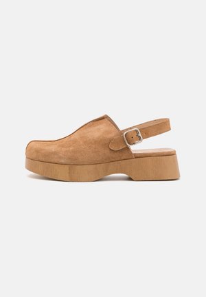 Tan suede slingback clog with wooden platform sole and adjustable silver buckle strap on white background.