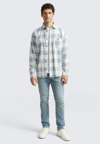 Wit en lichtblauw geblokt flanellen overhemd met knoopsluiting, voorzien van een enkele borstzak. Gecombineerd met een wit T-shirt, lichtgewassen jeans en sneakers.