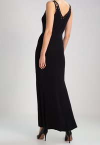 Abito maxi nero senza maniche con corpetto aderente, schiena a V e dettagli con cinturini a taglio. Realizzato in un materiale liscio e elastico, con una fessura laterale.