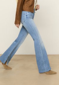 Lichtblauwe flared jeans met een hoge taille, voorzien van zijsplitten aan de zoom. De stof heeft een gladde textuur en een vervaagde gradient-afwerking.