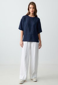 T-shirt in lino blu navy con scollatura ampia e maniche corte, abbinato a pantaloni larghi in lino bianchi e sneakers bianche. Design semplice, vestibilità rilassata.