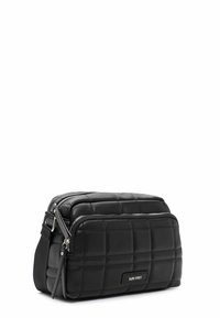 Sac bandoulière matelassé noir avec une forme rectangulaire, deux compartiments zippés et une sangle amovible pour plus de polyvalence. Fini texturé.