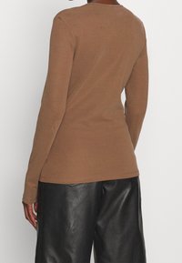 Brun långärmad topp i en åtsittande design, tillverkad av mjukt tyg. Har en rund halsringning och detaljer vid sid sömmar. Matchas med svarta läderbyxor.