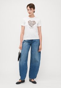 Witte t-shirt met korte mouwen, featuring een hartontwerp met luipaardprint en tekst, gecombineerd met ruime blauwe jeans en zwarte flats.