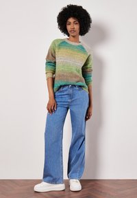 Sweter z dzianiny w zielone, kremowe i brązowe poziome paski; w zestawieniu z jasnoniebieskimi szerokimi dżinsami i białymi sneakersami.