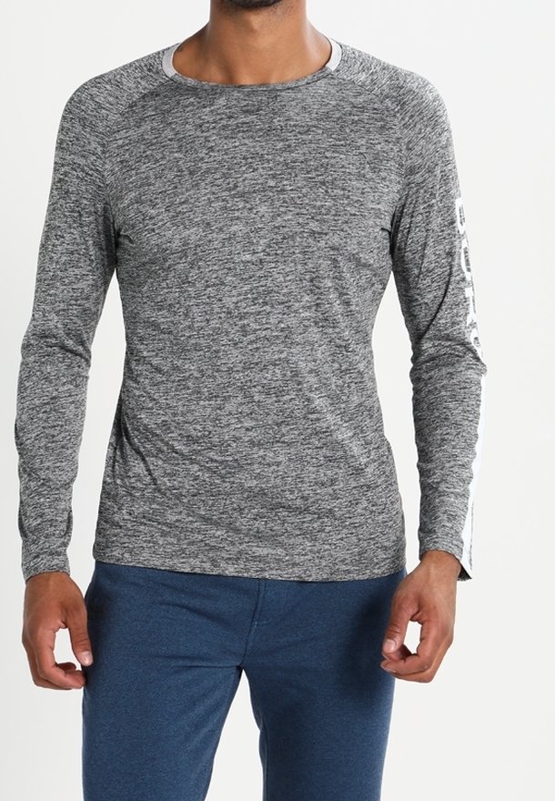 Man wearing a heather gray long-sleeve shirt with white text on one sleeve and blue pants, standing against a plain background.