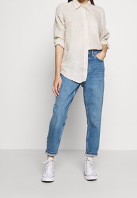 Vaaleanbeige pellavapaita napitettuna ja käännetyillä hihoilla, yhdistettynä löysiä sinisiin farkkuihin ja valkoisiin tennareihin.