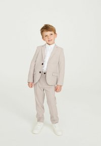 Completo grigio chiaro con giacca a due bottoni e pantaloni abbinati, completato da una camicia bianca e sneakers bianche. Tessuto morbido.