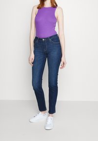 Top morado sin mangas combinado con jeans ajustados azul oscuro y zapatillas blancas. Tejido suave, silueta entallada y estilo clásico de denim.