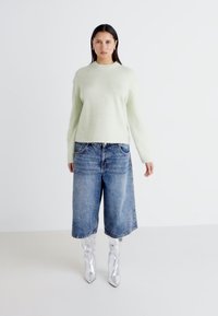 Lys grønn strikket genser med høy hals og avslappet passform. Vide blå denim culotter og sølvfargede knelang støvler med en shiny tekstur.