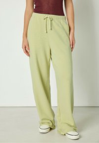 Svijetlozelene široke hlače od mekog, teksturiranog materijala, s elastičnim pojasom i vezicom. U kombinaciji s bijelim niskim tenisicama.