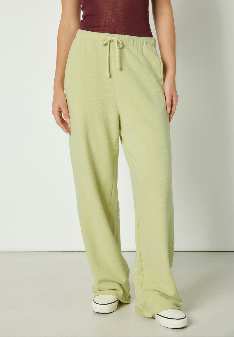 Svijetlozelene široke hlače od mekog, teksturiranog materijala, s elastičnim pojasom i vezicom. U kombinaciji s bijelim niskim tenisicama.