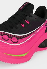 Μαύρο και λαμπερό ροζ αθλητικό παπούτσι με μαύρα κορδόνια, υφασμένο επάνω μέρος και νέον πράσινη λεπτομέρεια στη χοντρή σόλα, λοξή όψη που δείχνει πλαϊνές και μπροστινές λεπτομέρειες.