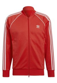 Red zip-up track jacket made of soft fabric, featuring white three-stripe accents on sleeves and a small Adidas logo on the chest.