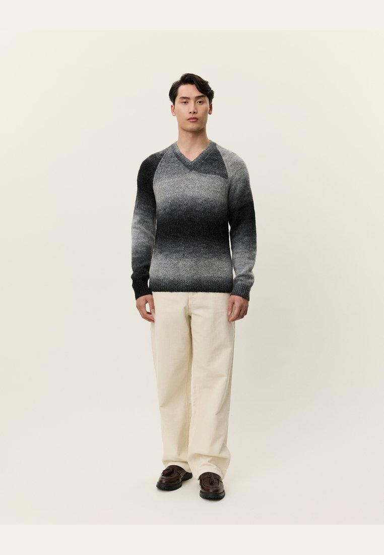 Pulover cu decolteu în V, în nuanțe de gri gradient până la negru, realizat dintr-un tricot texturat. Asortat cu pantaloni din catifea crem și pantofi întunecați.