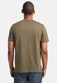 T-shirt verde oliva a maniche corte con una texture liscia, vestibilità classica e scollatura rotonda. Abbinato a jeans in denim blu.