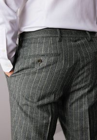 Grau gestreifte Hose mit taillierter Passform. Der strukturierte Stoff hat weiße Streifen und eine Gesäßtasche mit einem Knopfdetail.