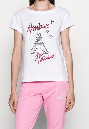 Kobieta nosząca białą koszulkę z szkicem Wieży Eiffla oraz czerwonym tekstem "Amour" i "Love Moschino,", połączona z różowymi spodniami z naszywką "Love Moschino".
