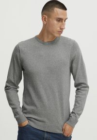 Grå strikkegenser med rund hals, lange ermer og ribbestrikkede mansjetter og nederkant. Glatt tekstur, minimalistisk design, uten synlige mønstre eller logoer.