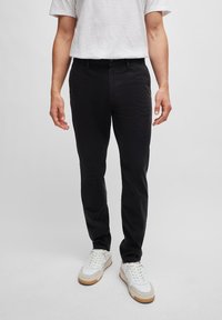 Mustat chinot, jotka on valmistettu puuvillasta ja joissa on slim fit -leikkaus. Niissä on vetoketjuhäntä, etutaskut ja ne on yhdistetty valkoisiin tennareihin. Yksinkertainen muotoilu, ei näkyviä kuvioita.