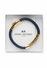 Navy flätad läderarmband med detaljer i guldtonad metall och en strukturerad stängning. Presenteras i en vit låda med varumärkeslogotyp.