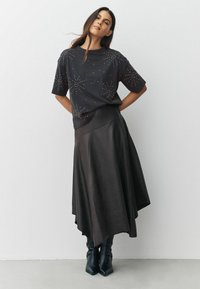 Zwarte t-shirt met korte mouwen en metalen studs, gecombineerd met een lange, vloeiende zwarte leren rok en zwarte enkelboots.