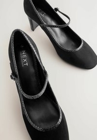 Crne suede visoke potpetice s Mary Jane trakicom, koje imaju glatku crnu unutrašnjost i teksturirani crni uzorak zmijske kože na trakici.