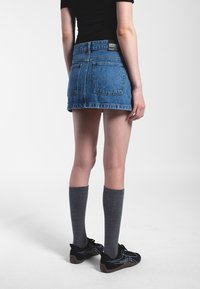 Mini gonna in denim blu con orlo sfilacciato, due tasche posteriori e un'etichetta del brand nera. Indossata con calze grigie fino al ginocchio e sneakers nere.