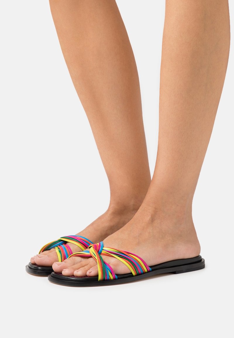 Des sandales à glissière multicolores présentent un design de lanière nouée en matériau texturé, reposant sur une semelle noire plate.