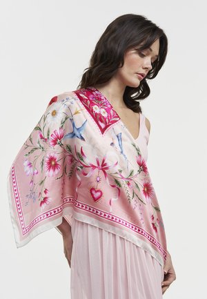 Tummahiuksinen nainen, jolla on vaaleanpunainen kukkakuvioinen huivi sinisillä linnuilla ja sydänkuvioilla, pukeutuneena vaaleanpunaiseen mekkoon, katsoo alaspäin.