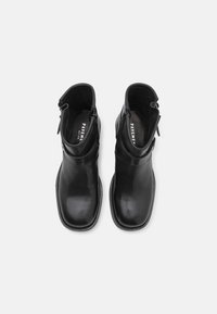 Paire de bottines en cuir noir à bouts carrés avec fermetures éclair latérales, vues de dessus sur fond blanc.
