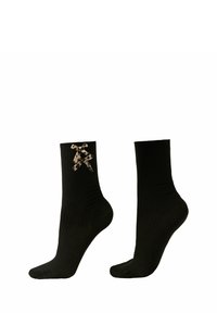 Calze nere a coste con una finitura testurizzata e un elegante motivo a fiocco decorativo sulla caviglia. Elasticizzate per una vestibilità aderente.