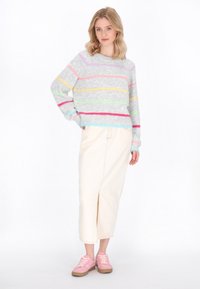 Maglione grigio a righe con strisce pastello rosa, gialle, verdi e blu; gonna midi color crema con uno spacco anteriore; sneakers rosa con suola color beige.