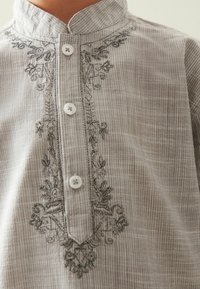 Grårandig skjorta med en halva placket, tre knappar och intrikata svarta blommor broderade längs halsringningen. Slät tygtextur.