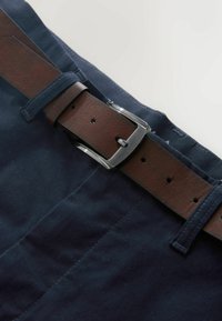 Kék pamut nadrág barna bőr övvel. Az öv ezüstszínű fémcsattal és több állítható lyukkal rendelkezik. Az anyag sima tapintású.