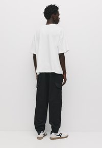 Witte oversized t-shirt met korte mouwen, gecombineerd met losse zwarte cargobroek met zijzakken. Schoenen: witte sneakers.